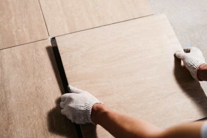 Des mains gantées pour installer un revêtement de sol en carreaux de céramique