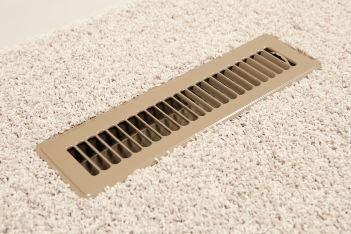 Grille d'aération dans un plancher avec moquette beige.