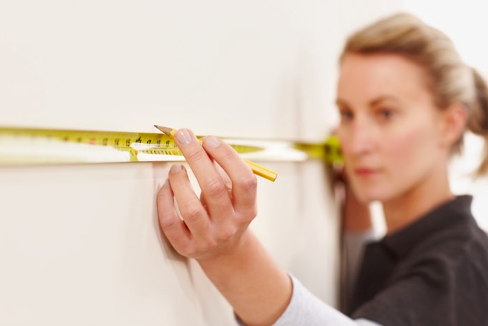 Une femme utilise un mètre ruban pour mesurer le mur à 16 pouces de l'angle.