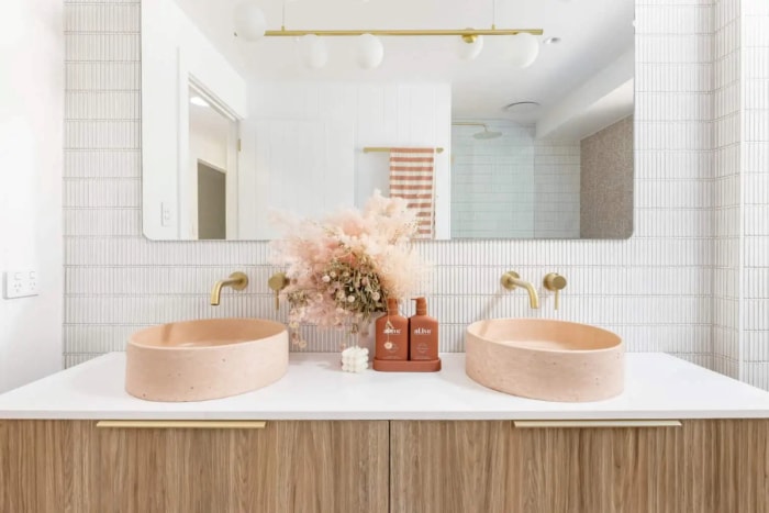 Salle de bain avec luminaires dorés et lavabos en pierre rose.