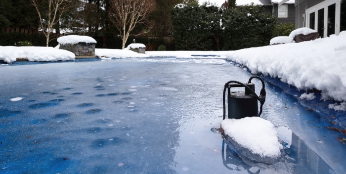 Une pompe de piscine est recouverte de neige et de glace au bord d'une piscine gelée.