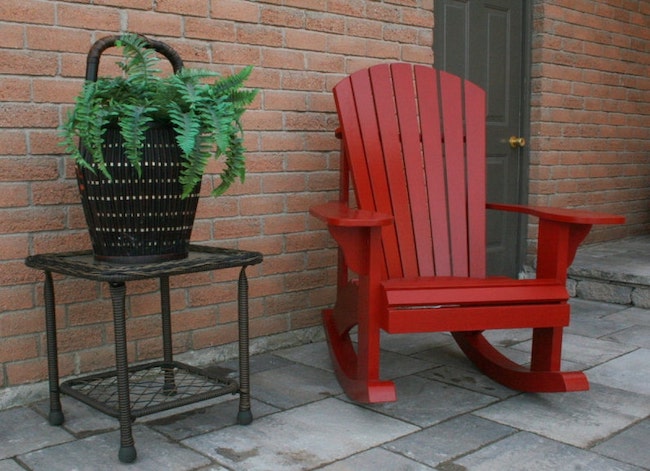 Chaise à bascule Adirondack rouge à côté d'une table de patio avec plante