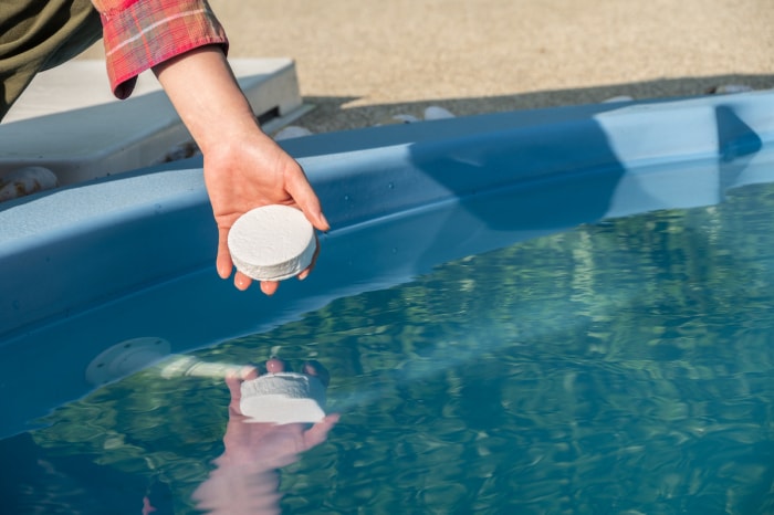 Une personne place une tablette de chlore dans une piscine.