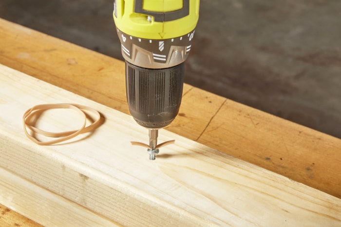 Une personne utilise un élastique pour retirer une vis dénudée encastrée dans un poteau en bois.