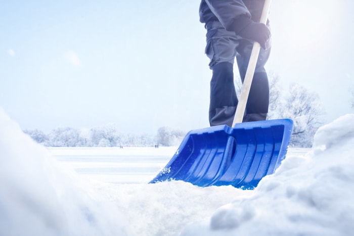 Une personne utilise une pelle bleue pour balayer la neige.