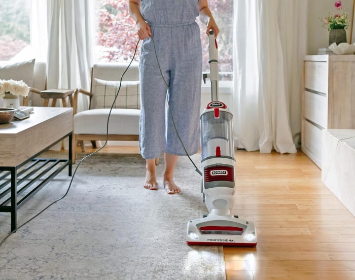 Une femme utilise un aspirateur vertical professionnel Shark Rotator Lift-Away pour aspirer un tapis sur un plancher de bois franc.