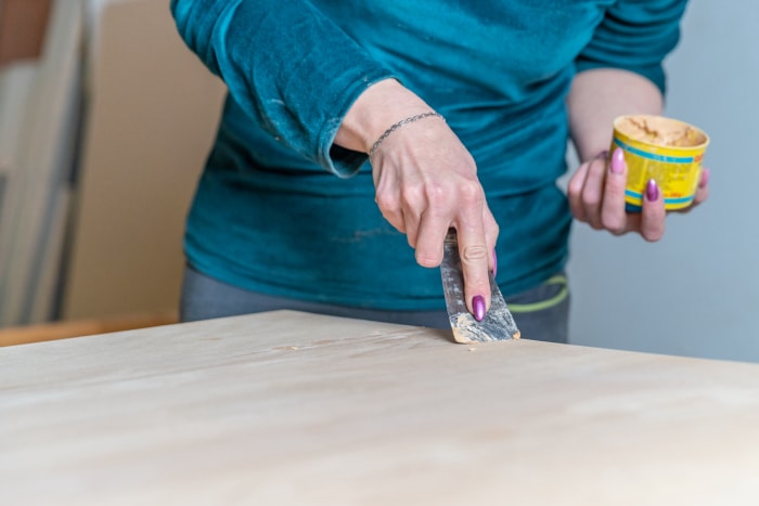 Les mains d'une personne appliquent de la pâte à bois sur la surface d'une table.