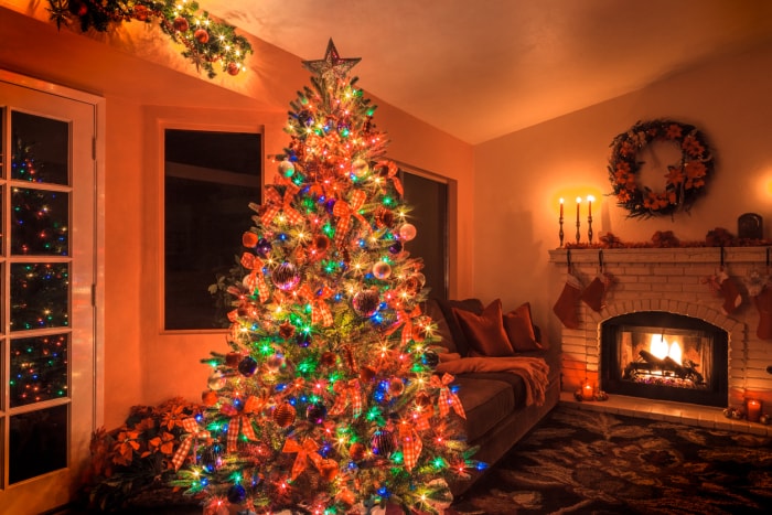 Un arbre de Noël avec de nombreuses lumières multicolores brille dans un salon avec cheminée.