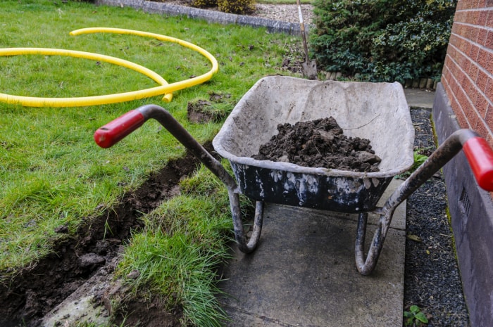 Brouette pleine de terre après qu'une tranchée ait été creusée au fond d'une pelouse pour installer un canal de drainage.