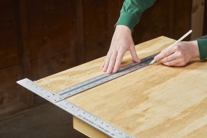 Une femme mesure et marque une planche de contreplaqué.