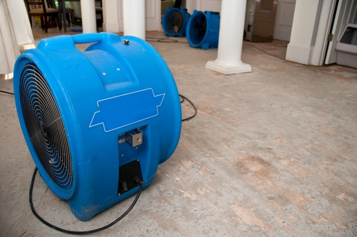 Un grand ventilateur de sol bleu pour sèche-linge utilisé dans le sol humide d'un sous-sol.