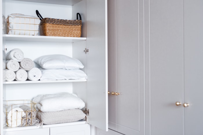 Linge blanc, oreillers, serviettes organisés et pliés dans des paniers sur des étagères dans un placard à linge blanc ouvert dans la salle de bain.