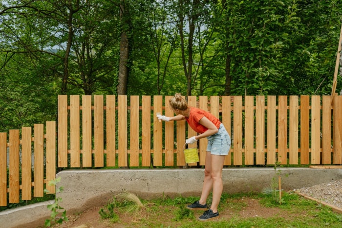 Une femme peint une clôture en bois. 