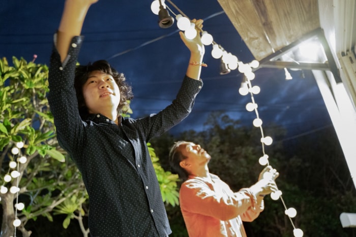 Deux hommes d'origine asiatique travaillent ensemble pour installer des guirlandes lumineuses à l'extérieur d'une maison