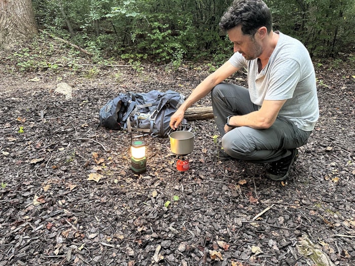 Une personne utilisant un réchaud de camping dans les bois à côté de la meilleure option de lanterne LED