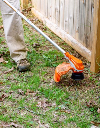 Personne utilisant une débroussailleuse à batterie Stihl FSA 80 R pour couper l'herbe le long d'une clôture en bois