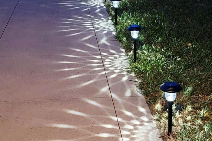 Trois éclairages solaires noirs pour le chemin qui projettent une lueur décorative à motifs sur le chemin la nuit.