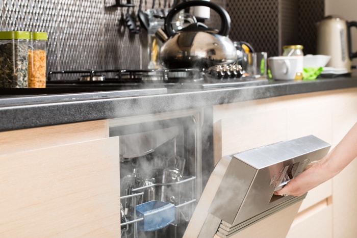 Ouverture d'un lave-vaisselle après un cycle de lavage à chaud, laissant échapper de la vapeur dans une cuisine