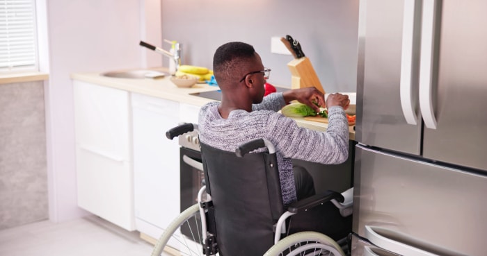 Une personne est assise dans un fauteuil roulant qui se place sous un comptoir de cuisine tout en préparant la nourriture.