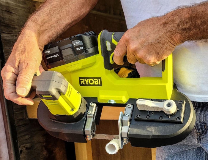 Une personne utilisant le kit de scie à ruban sans fil Ryobi P590K1 One+ 18 V pour couper un morceau de tuyau en PVC pendant les tests.