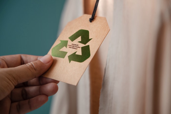 Une personne tenant une étiquette de prix avec les mots « fabriqué à partir de matériaux 100 % recyclés » dessus.