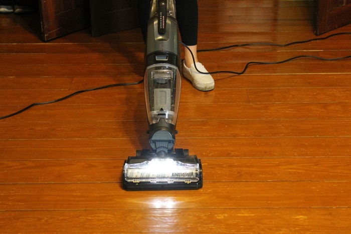 Personne nettoyant un plancher de bois franc avec un aspirateur eau et poussière Bissell crosswave gris