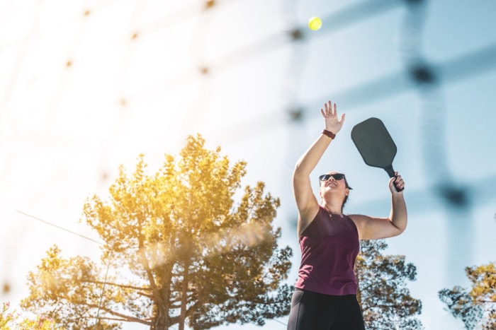 Une personne sert un pickleball au soleil.