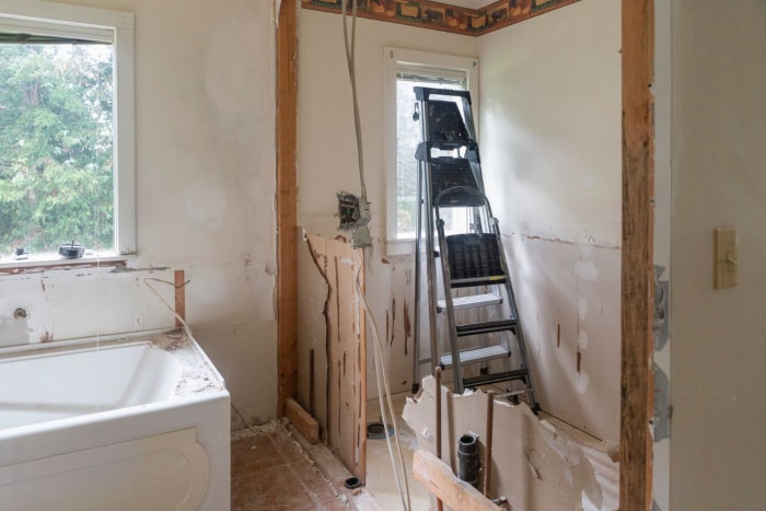 Une salle de bains a été démolie pour être rénovée. Il reste une vieille baignoire et une échelle appuyée contre la fenêtre.