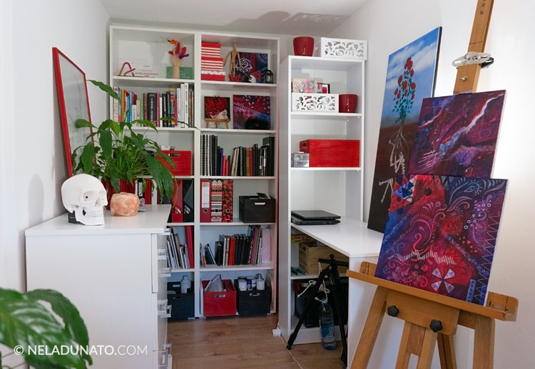 Atelier d'art au décor rouge et blanc posé sur une grande bibliothèque derrière un chevalet.