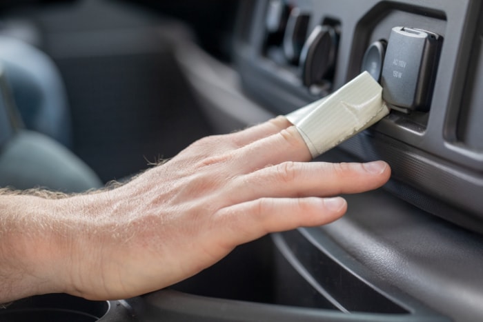 Main avec du ruban adhésif autour des doigts pour nettoyer les boutons de la voiture.