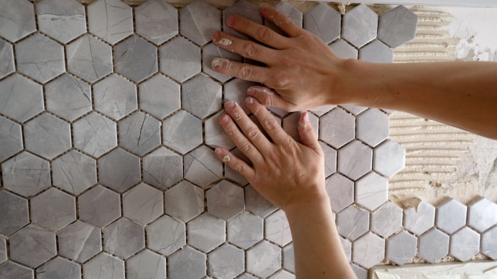 Une personne pose du carrelage hexagonal gris sur le mur d’une salle de bain.