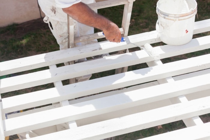 Gros plan d'un professionnel utilisant un petit rouleau à peinture pour appliquer de la peinture blanche sur une terrasse en bois.