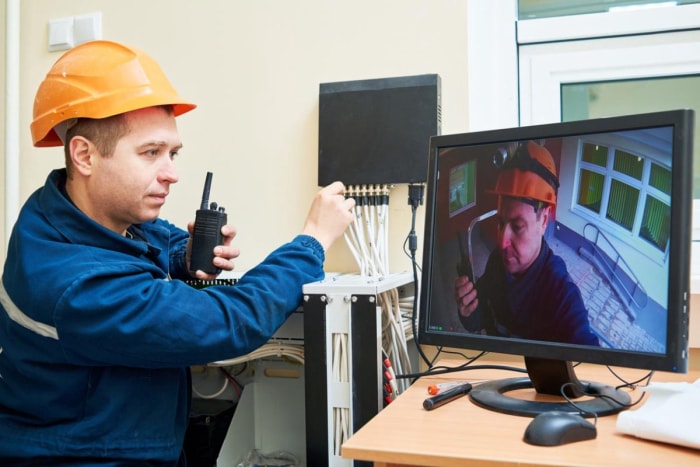 Un travailleur portant un casque de sécurité orange évalue le flux vidéo d'un système de sécurité. 