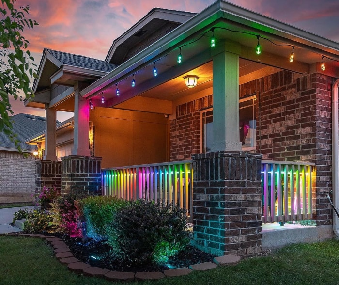 devant la maison avec porche éclairé aux couleurs de l'arc-en-ciel par des guirlandes lumineuses