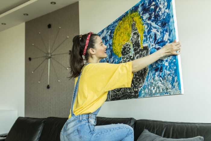 iStock-1311835719 décoration avec une femme artisanale accrochant une peinture abstraite bleue et jaune sur un mur