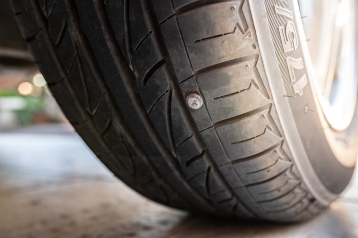 Gros plan sur un clou ou une vis collée sur le pneu de la voiture