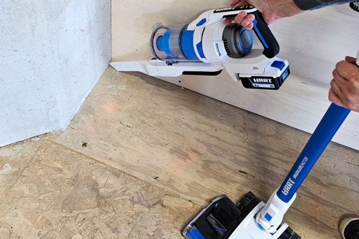 Une personne utilise l'aspirateur à manche sans fil Hart pour enlever la poussière et la saleté dans un coin d'une zone de travail.