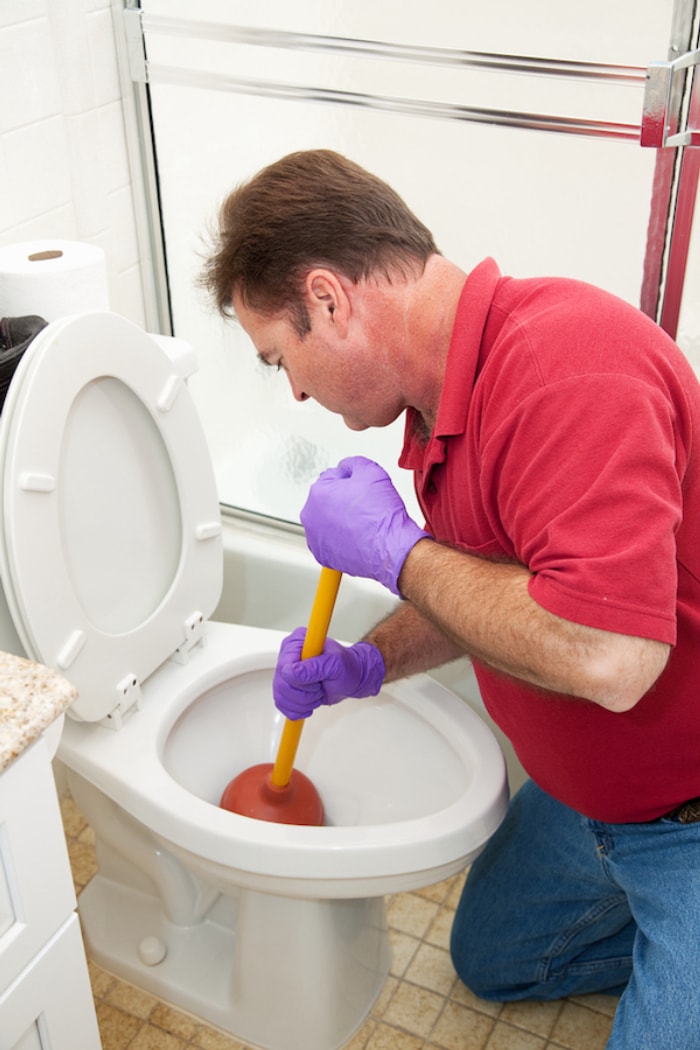 homme portant des gants en caoutchouc plongeant dans les toilettes