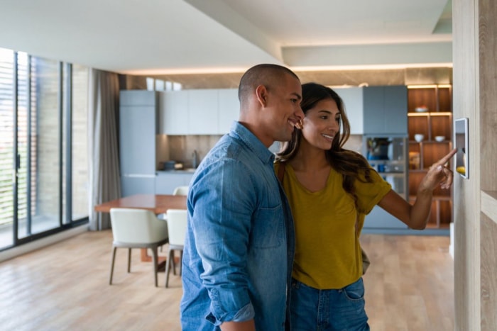 Un couple vérifie le panneau de contrôle de sécurité de leur maison dans une cuisine. 