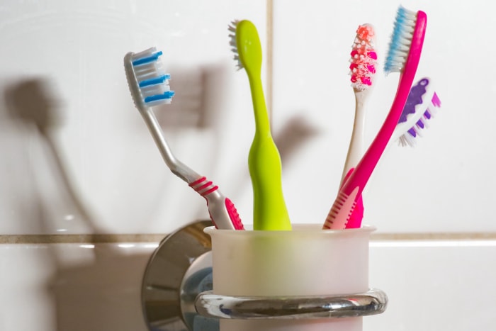 Cinq brosses à dents colorées sont conservées dans un gobelet à brosses à dents dans la salle de bain.