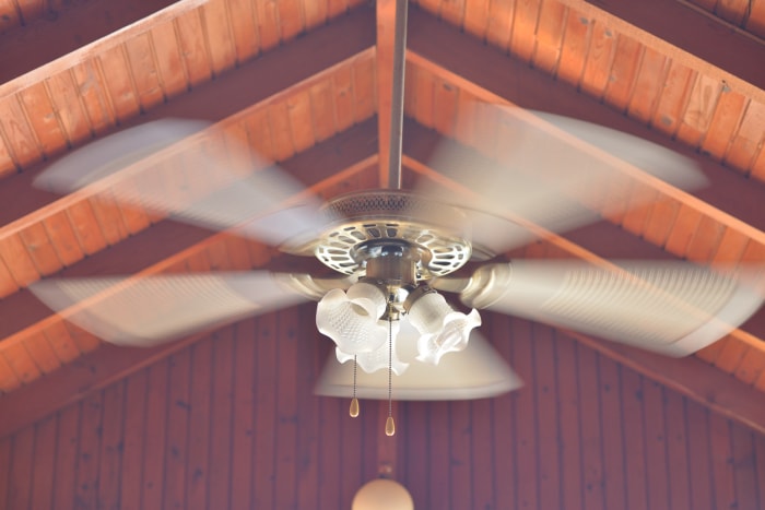 Un ventilateur de plafond monté sur un plafond voûté en bois a des chaînes de traction courtes.