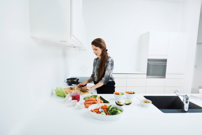 Femme cuisinant avec des ingrédients colorés dans une cuisine blanche.