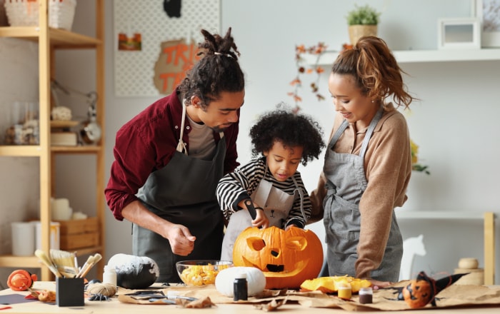 Heureuse mère, père et fils d'une famille ethnique sculptant ensemble une citrouille pour les vacances d'Halloween, se préparant pour la fête de fin d'année dans la cuisine, s'amusant tout en créant une citrouille-lanterne