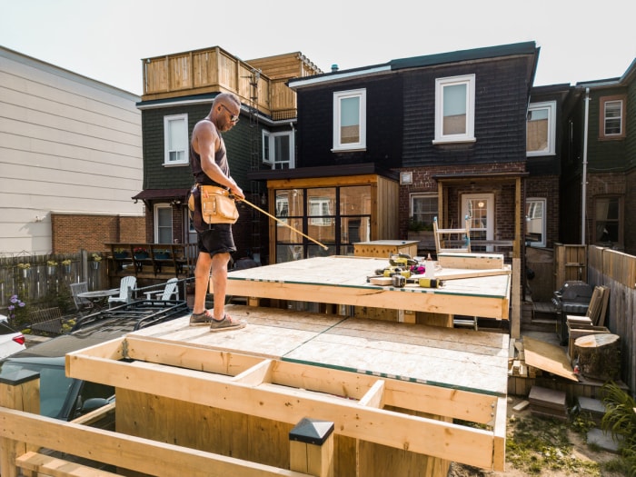 un ouvrier prend les mesures d'une terrasse partiellement construite derrière une maison avec un revêtement noir