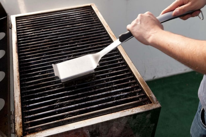 Une personne utilise la meilleure brosse à grillades pour nettoyer les grilles de cuisson d'un grill.