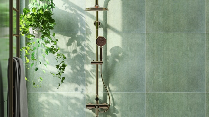 De grands carreaux carrés vert sauge recouvrent le mur d'une douche avec une plante.