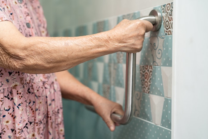 le bras d'une femme âgée saisit une barre de sécurité dans une salle de bain carrelée