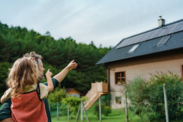 iStock-1431921497 types de peinture vue d'oreille d'un père tenant sa petite fille dans les bras et montrant leur maison avec des panneaux solaires installés