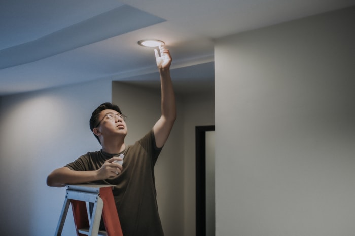 Un homme sur une échelle change l'ampoule LED du plafonnier.