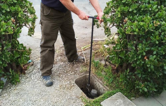 Un homme utilise une clé à eau pour accéder aux conduites d'eau à l'extérieur de sa maison.